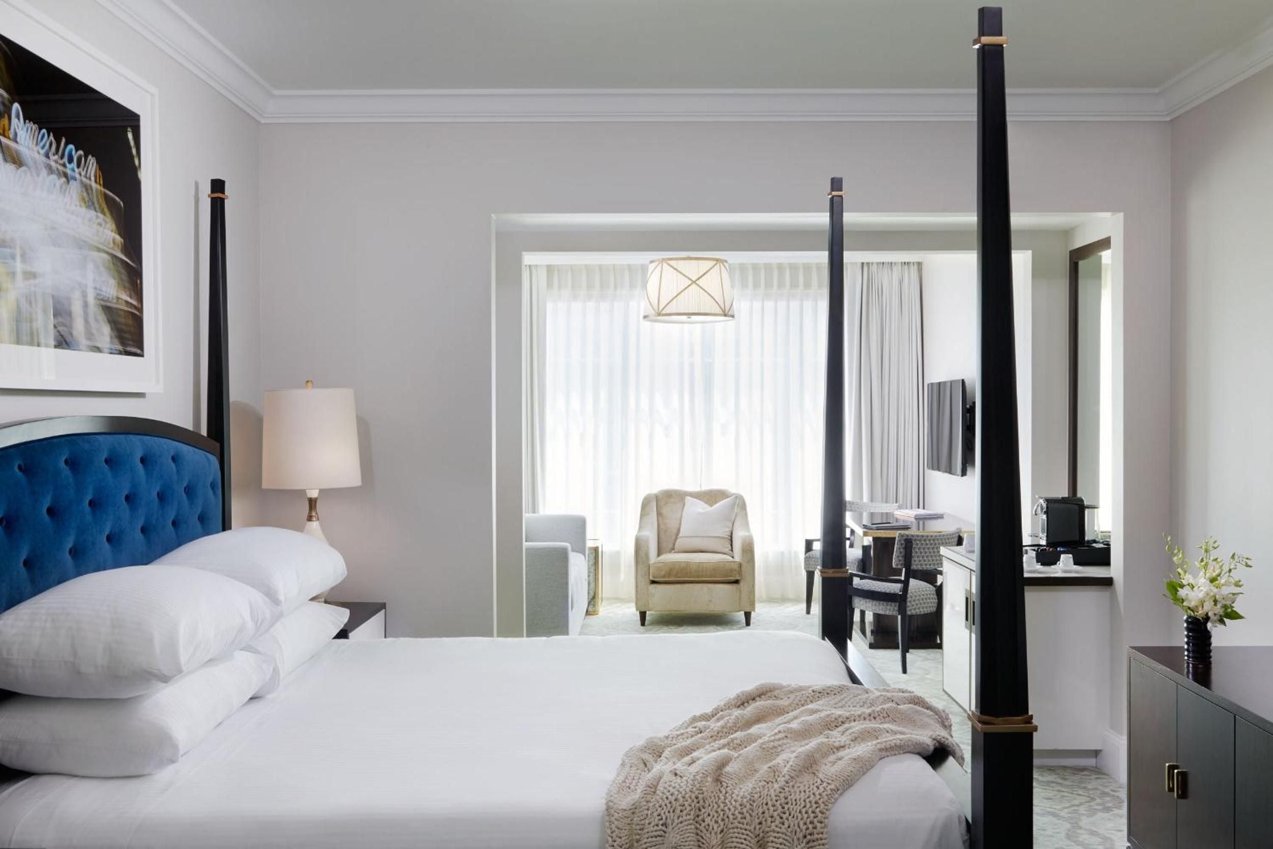 Crisp white linens contrast beautifully with the sapphire velvet headboard, while black four-poster details add sophisticated drama to this light-filled corner suite.