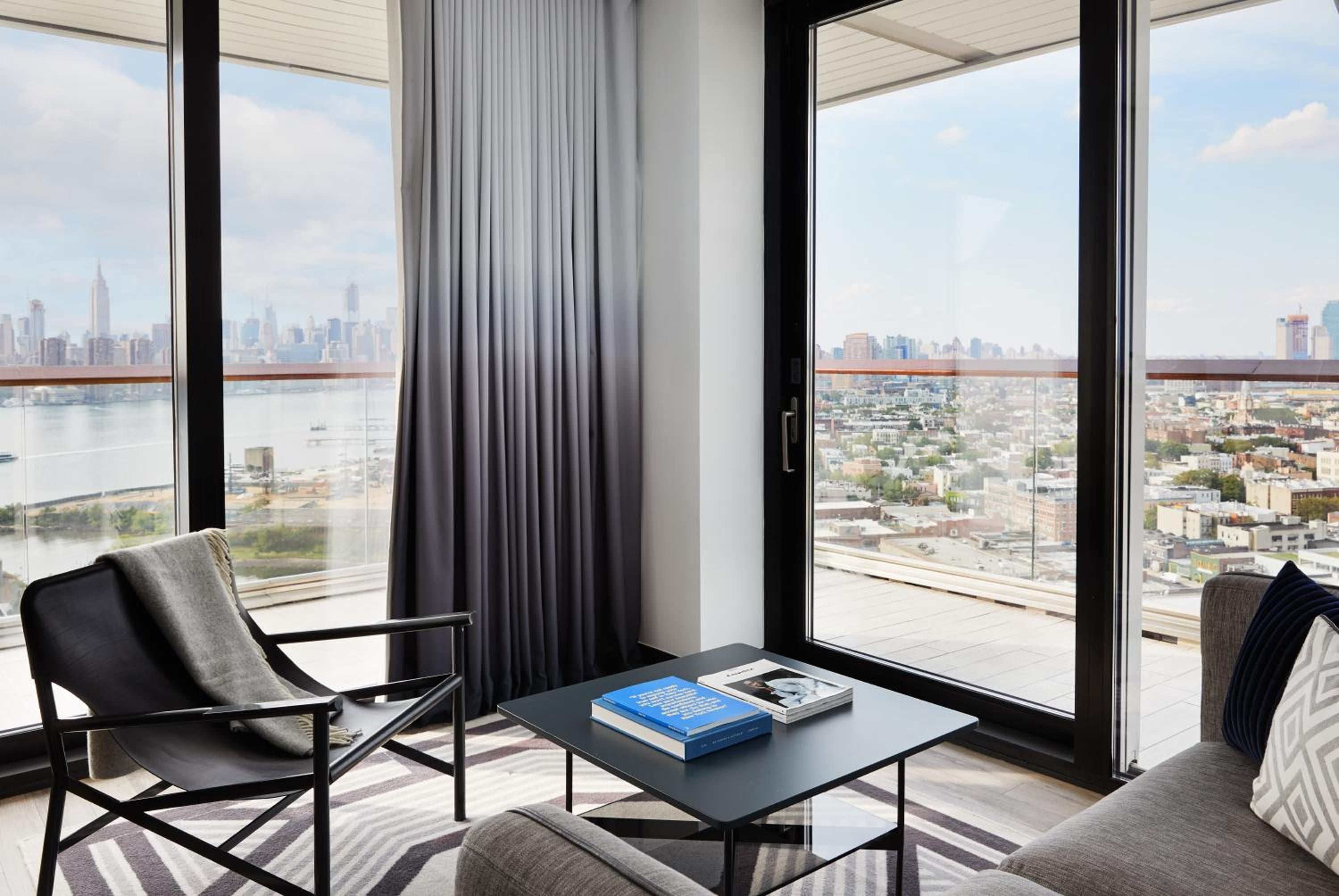 Floor-to-ceiling windows frame Manhattan's glittering skyline from this corner suite, where charcoal furnishings and crisp linens create an urban sanctuary above Brooklyn's waterfront.