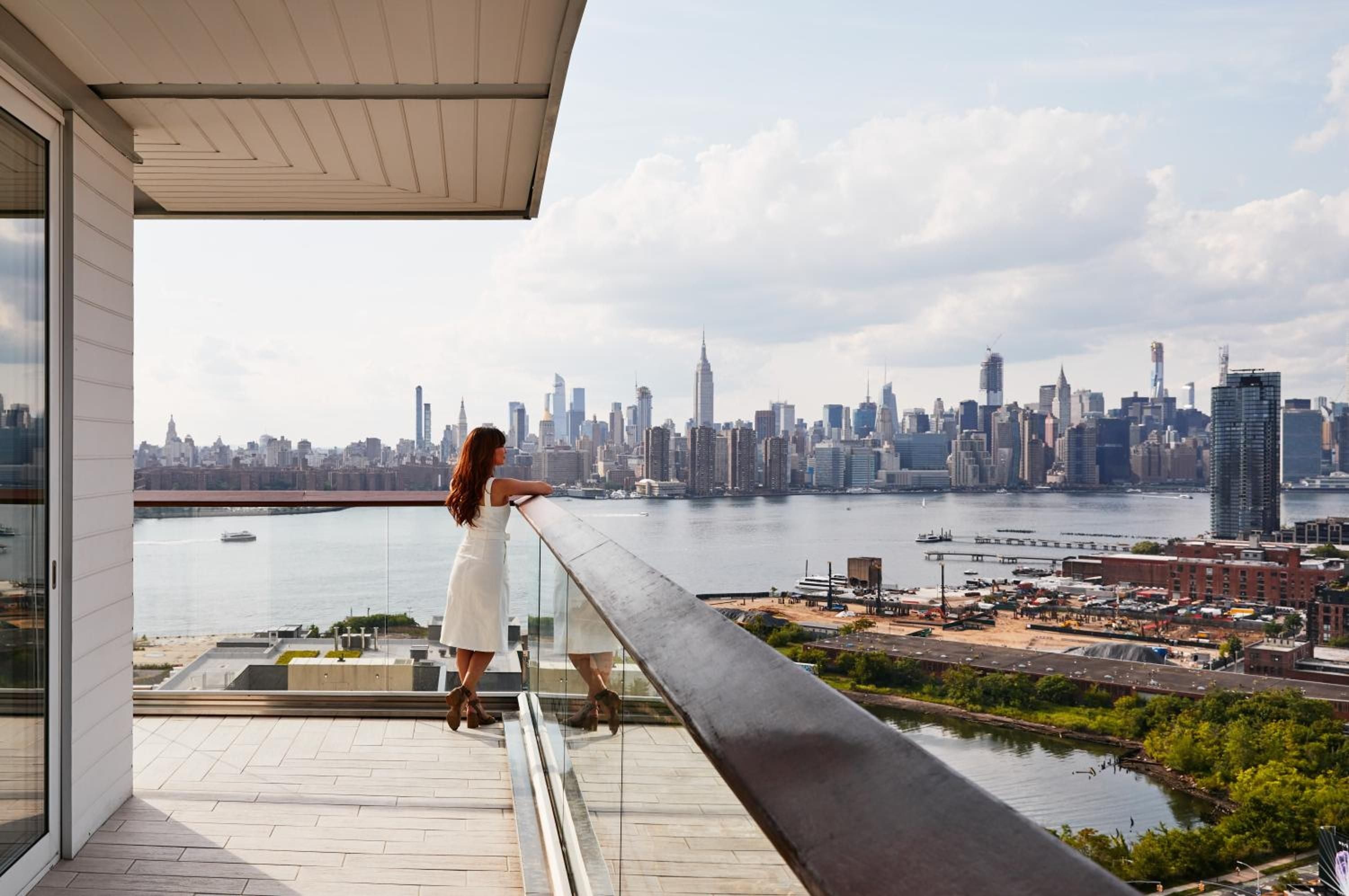 Manhattan's iconic skyline unfolds across the Hudson River from a private terrace, where floor-to-ceiling glass and warm stone create an intimate viewing perch above Brooklyn's waterfront.