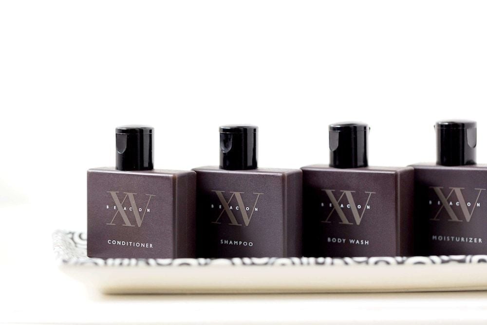 Sleek XV Beacon amenities lined up like dark jewels on marble—conditioner, shampoo, body wash, and moisturizer promising indulgent moments in this sophisticated Boston retreat.