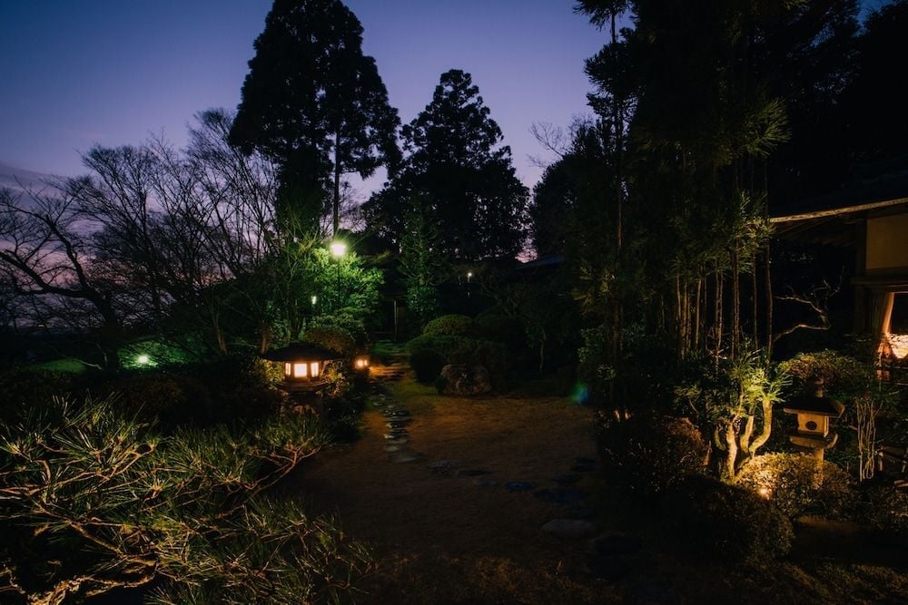 Stone lanterns cast golden pools of light along winding pathways through Yoshida-sanso's traditional gardens, where twilight transforms ancient cedars into silhouettes against the deepening sky.