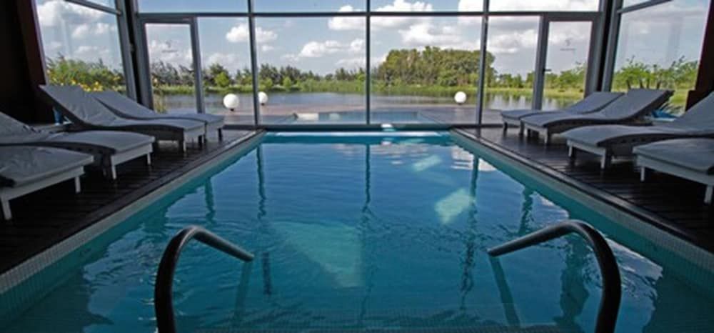 Floor-to-ceiling windows frame verdant countryside views while you float in the crystalline indoor pool, where tranquility meets sophisticated design beneath soaring glass ceilings.