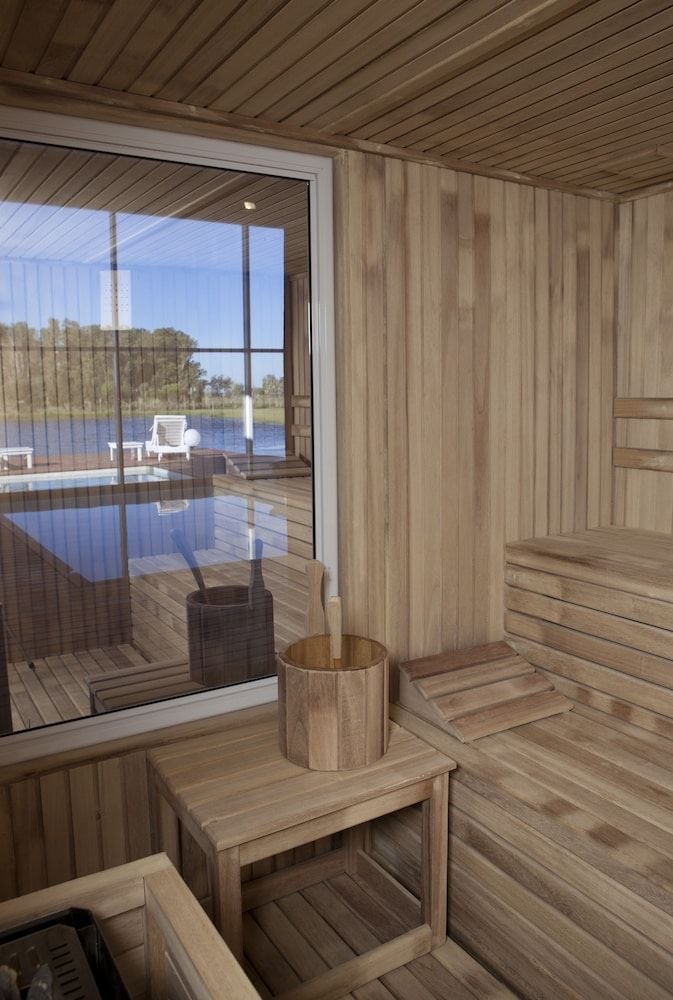 Warm cedar envelops you in the Finnish-style sauna, where traditional wooden buckets and benches overlook tranquil water views through floor-to-ceiling windows.