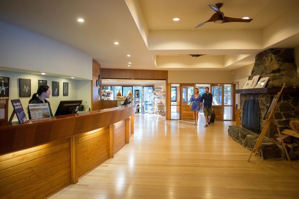 Warm timber reception desk and soaring ceilings create an inviting arrival experience, while dramatic stone fireplace anchors this mountain lodge-style lobby with rustic elegance.
