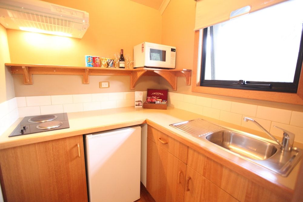 Warm timber cabinetry and compact efficiency define the lodge's kitchenette, where golden light streams through porthole windows onto honey-toned wood surfaces.