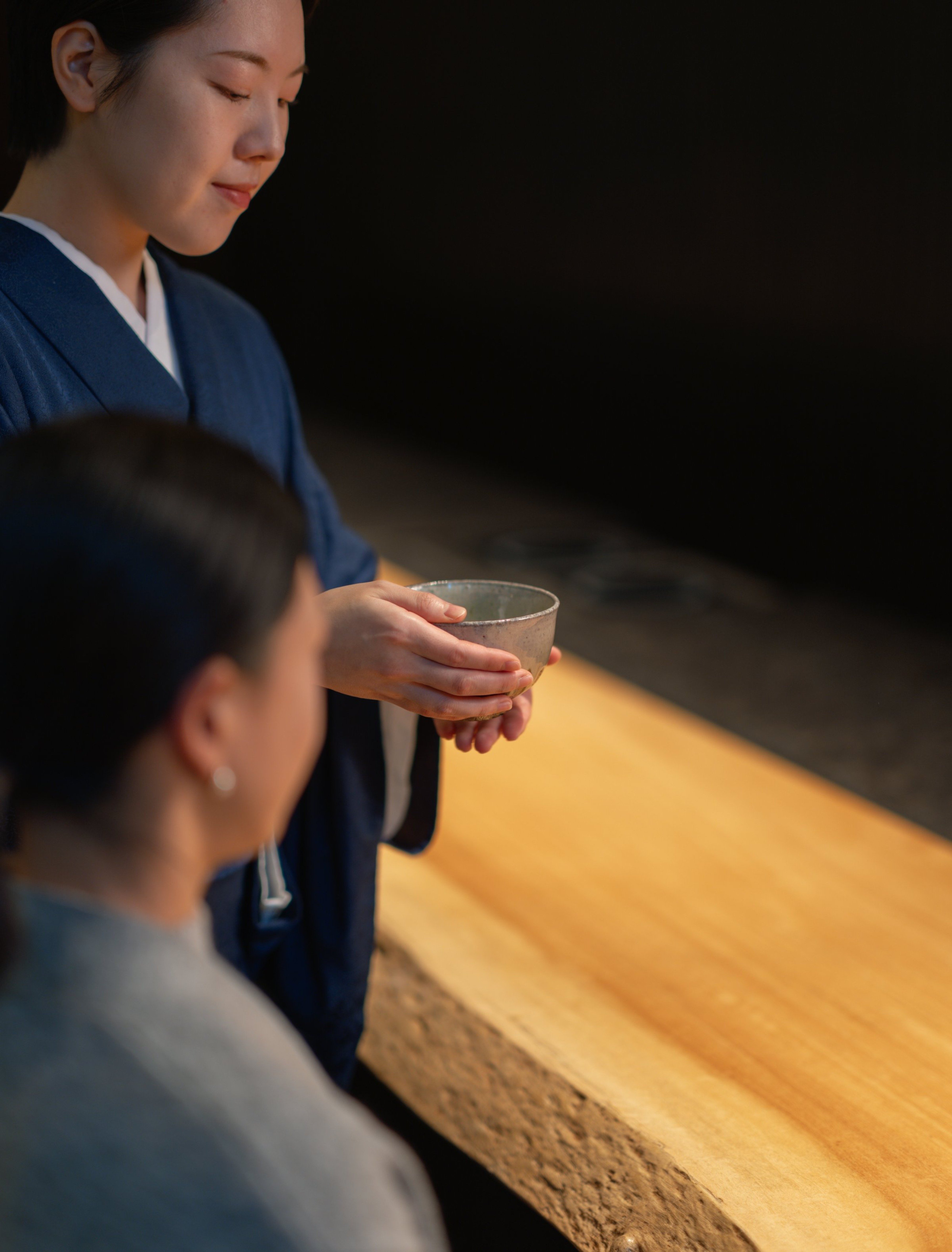 Gentle hands cradle handcrafted ceramics as warm golden light illuminates traditional Japanese hospitality, creating moments of profound tranquility in Aman's serene treatment spaces.