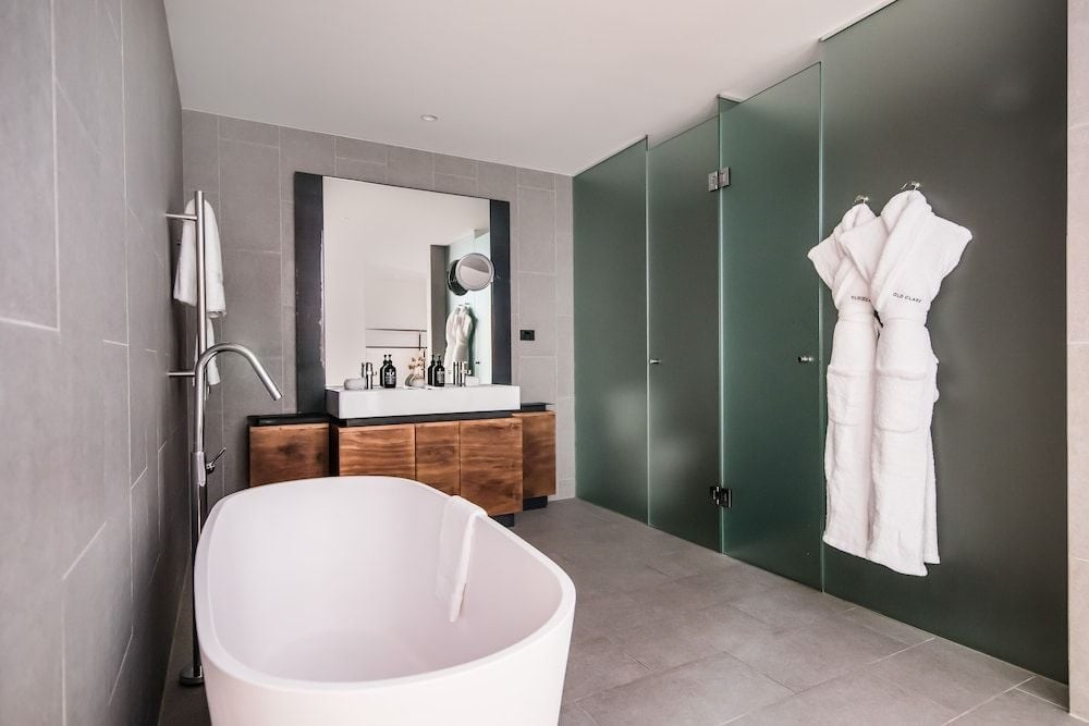 Sage-green glass panels and warm walnut vanities create a sophisticated sanctuary, where the sculptural freestanding tub becomes an invitation to unwind in style.