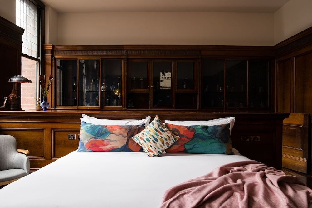 Rich timber paneling and vintage glass cabinets frame the bed, where vibrant abstract pillows add contemporary flair to this thoughtfully restored heritage space.