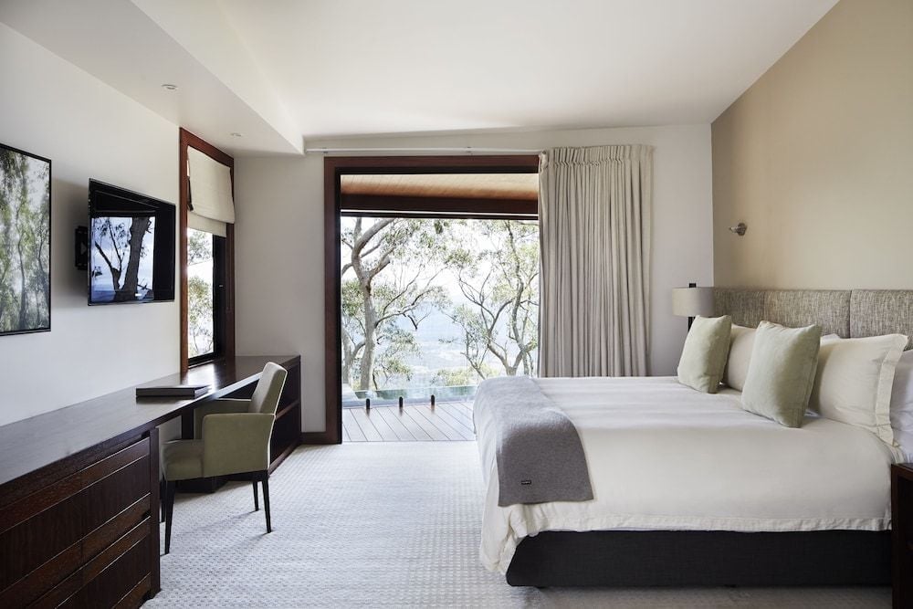 Floor-to-ceiling windows frame ancient eucalyptus trees while neutral linens and warm timber create a serene retreat above the Scenic Rim's rolling valleys.