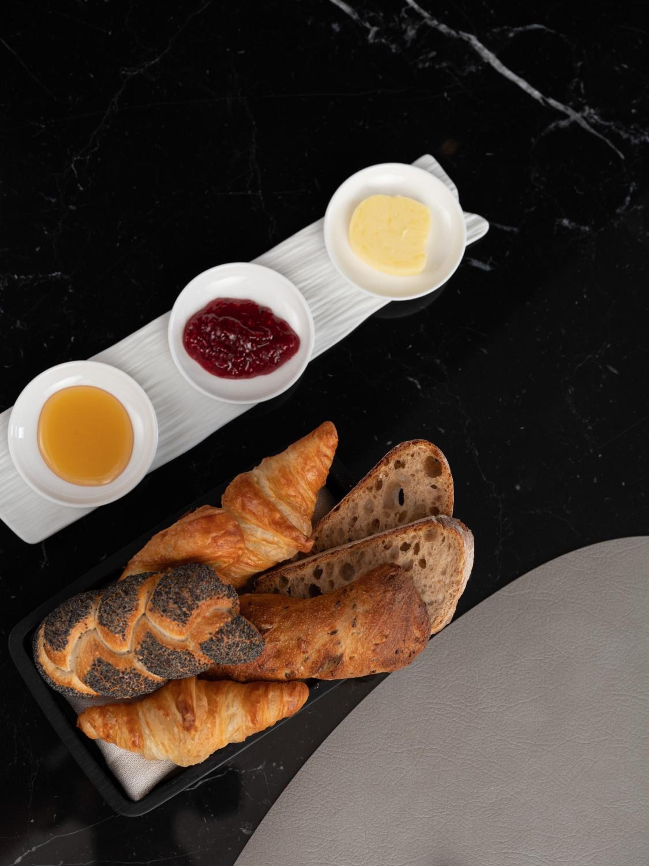 Artisanal breads and house-made preserves arrive on sleek marble surfaces, where golden honey and ruby jam create an elegant morning ritual of refined simplicity.