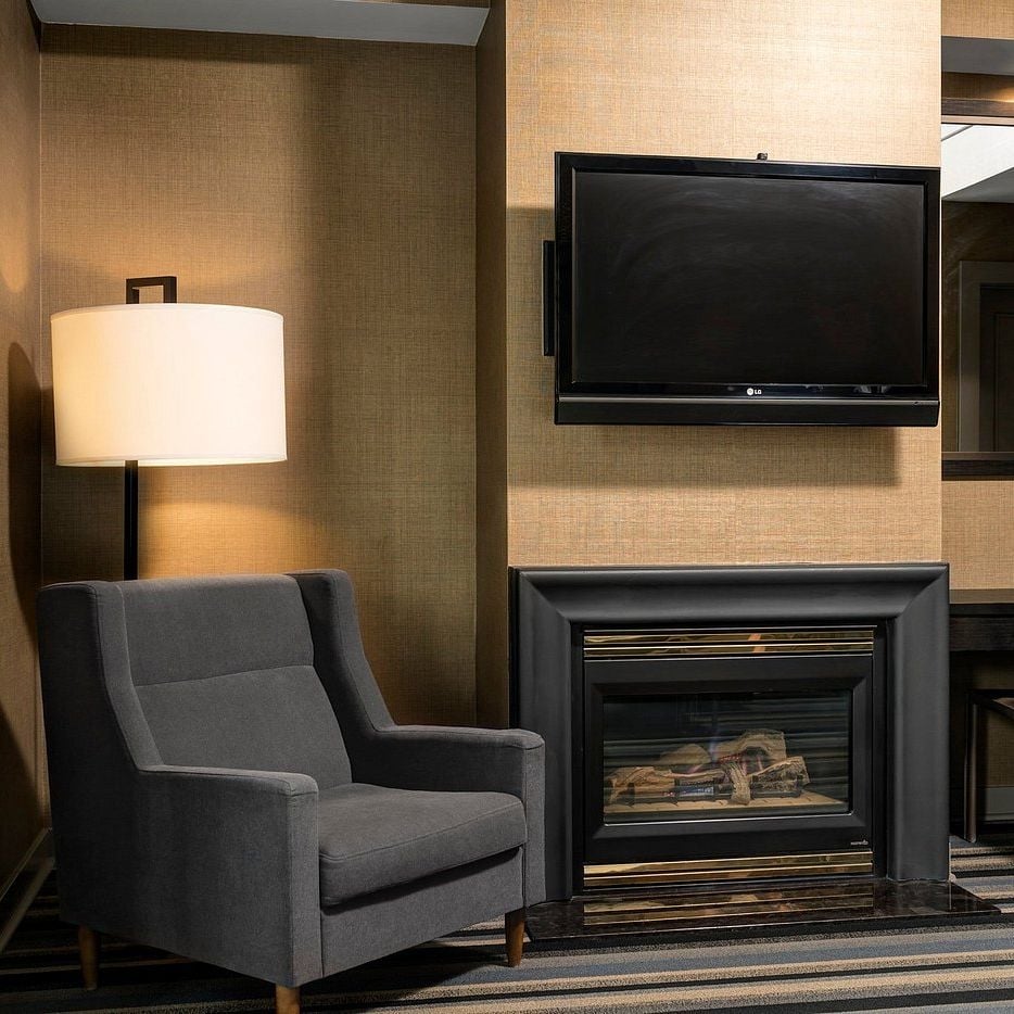 Charcoal armchairs and warm textured walls create intimate conversation nooks, where modern fireplaces cast a golden glow perfect for evening relaxation.