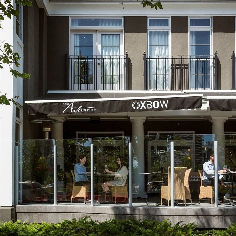 Floor-to-ceiling windows blur the line between sidewalk and dining room, where guests savor intimate conversations over leisurely meals in wicker chairs.