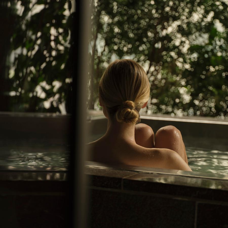 Dappled sunlight filters through verdant foliage as steam rises from the Japanese-inspired soaking tub, creating an urban sanctuary of profound tranquility.