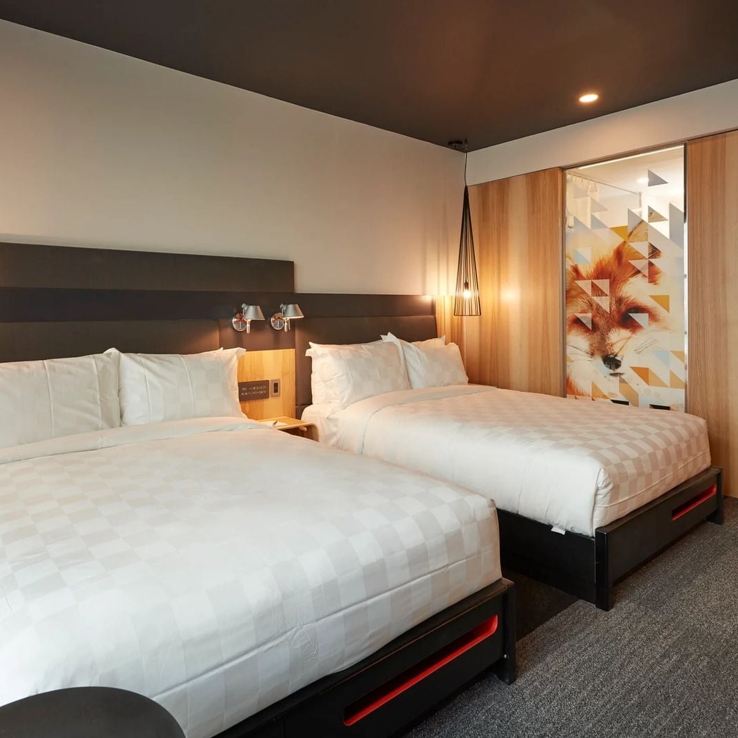 Warm wood accents and geometric artwork create intimate ambiance in these twin queen rooms, where pendant lighting casts golden pools across crisp white linens.