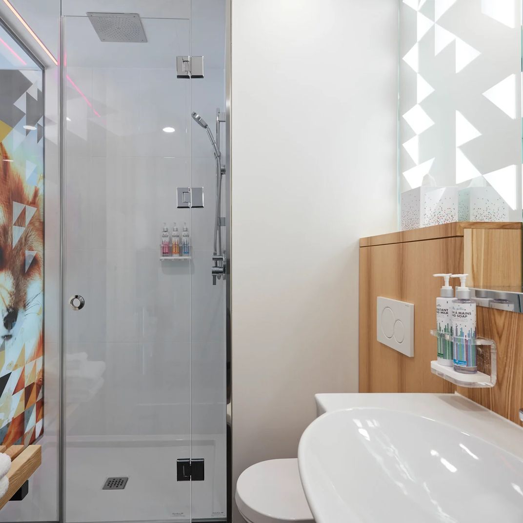 Sleek glass enclosures and warm wood vanities create spa-like serenity in compact quarters, where geometric window patterns cast playful shadows across pristine surfaces.