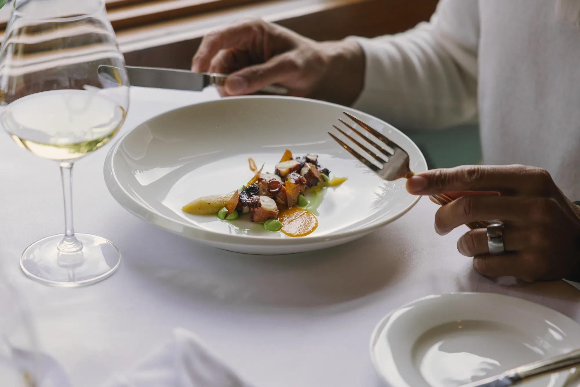 Artfully plated seasonal ingredients arrive at your table alongside crisp white wine, where natural light illuminates each carefully composed bite in the hotel's refined dining room.