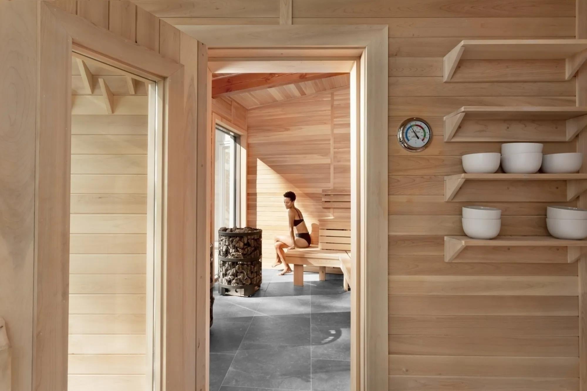 Natural light floods the cedar-lined sauna where handcrafted wooden shelves hold ceramic bowls and a traditional thermometer monitors the perfect Nordic heat.
