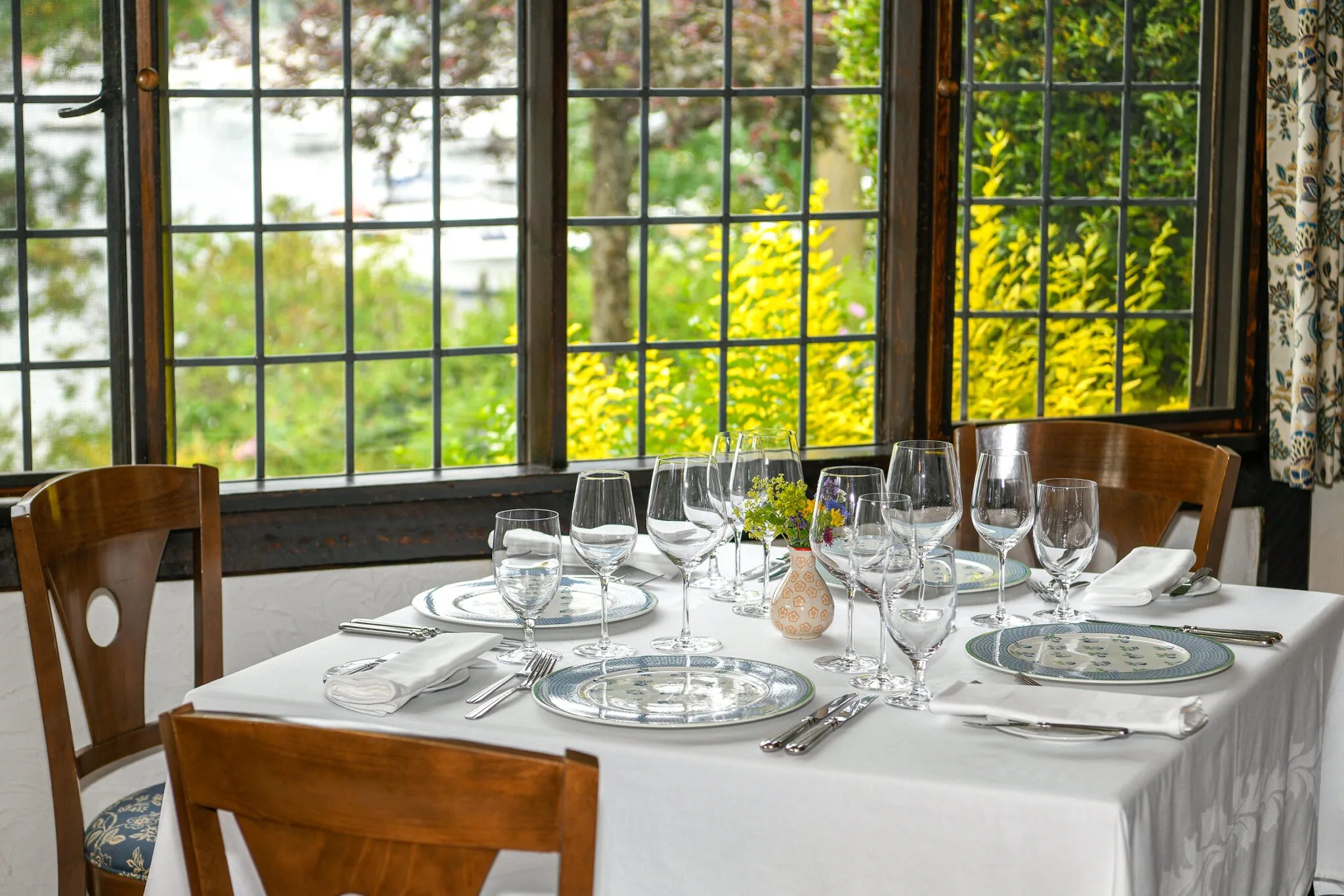 Sunlight streams through diamond-paned windows onto crisp linens and gleaming crystal, where garden views frame an intimate dining experience steeped in country elegance.
