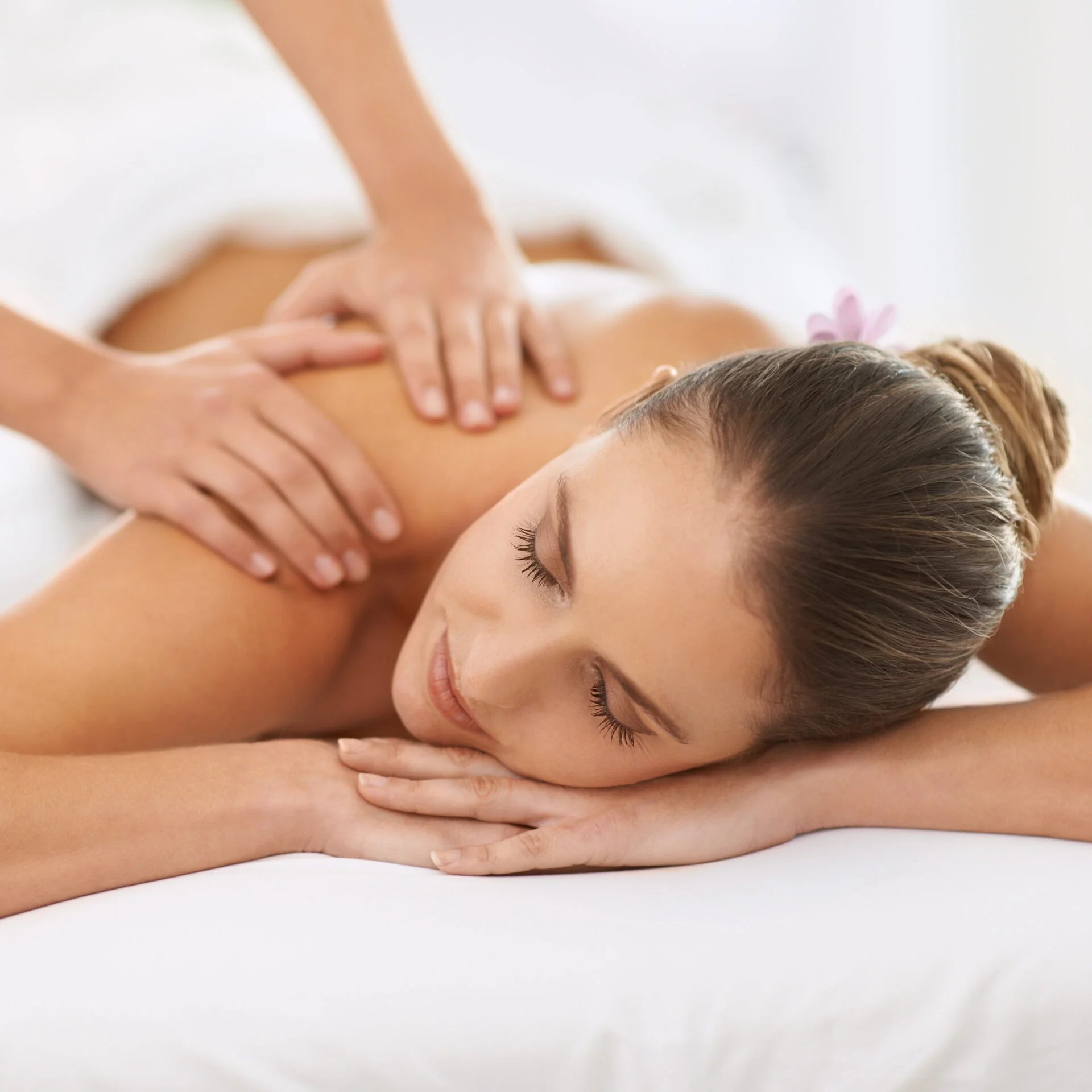 Skilled hands work tension from shoulders as soft natural light creates a cocoon of tranquility in the spa's serene treatment rooms.