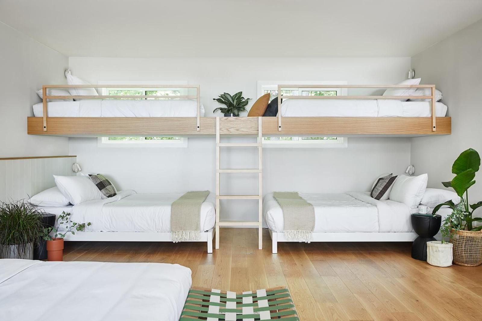 Scandinavian-inspired bunk beds with warm wood frames and crisp white linens create a serene shared sanctuary, enhanced by trailing plants and soft natural light.