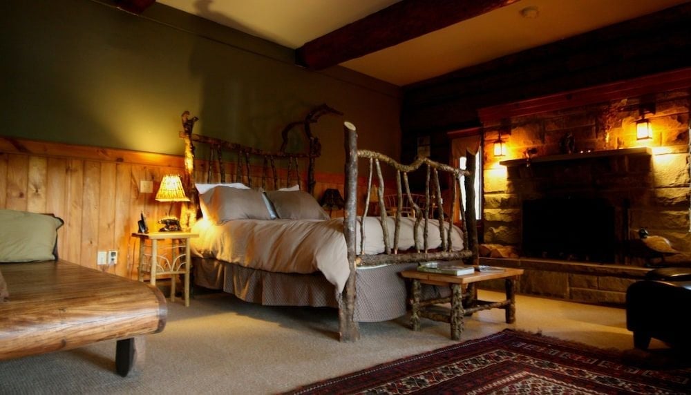 Rustic birch four-poster beds and stone fireplaces create an intimate wilderness retreat, where exposed beams and warm lamplight enhance the lodge's authentic Nova Scotia charm.