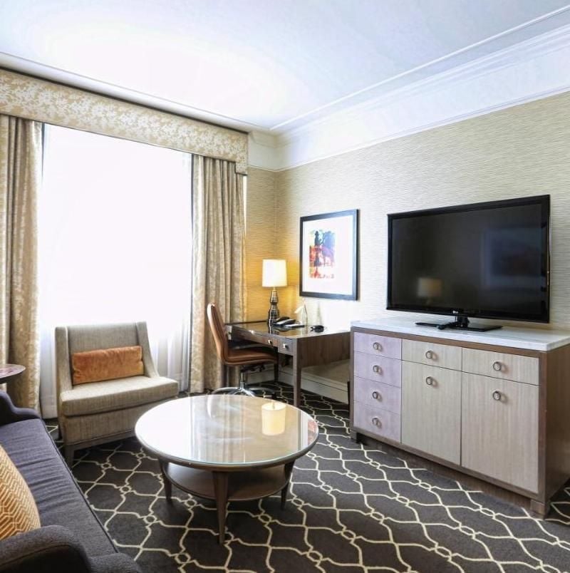 Geometric carpeting in rich charcoal anchors this sophisticated suite, where gleaming marble surfaces meet warm wood furnishings beneath soaring coffered ceilings.