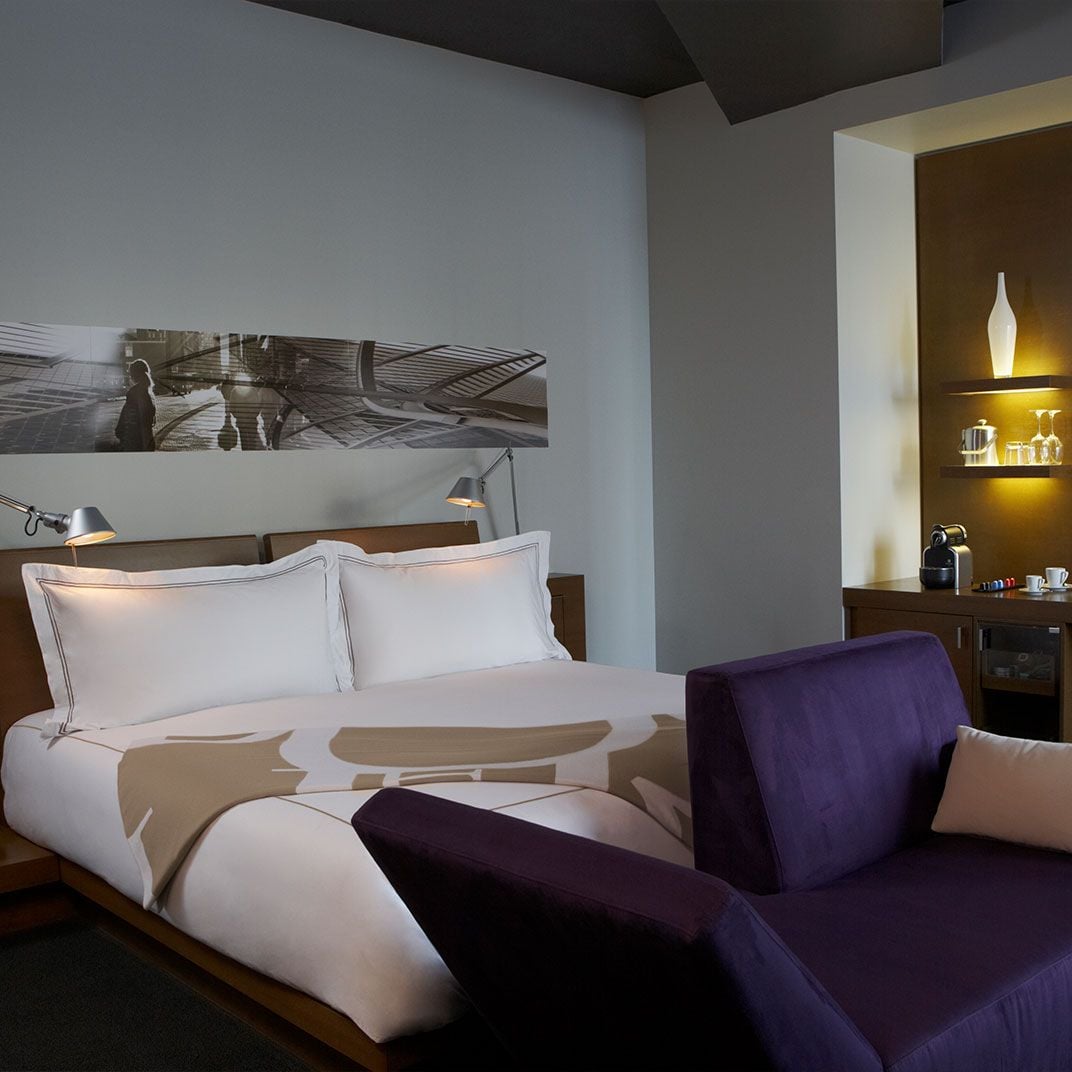 Warm amber lighting illuminates a sleek alcove bar while contemporary artwork and purple velvet seating create intimate sophistication in this thoughtfully designed guest room.