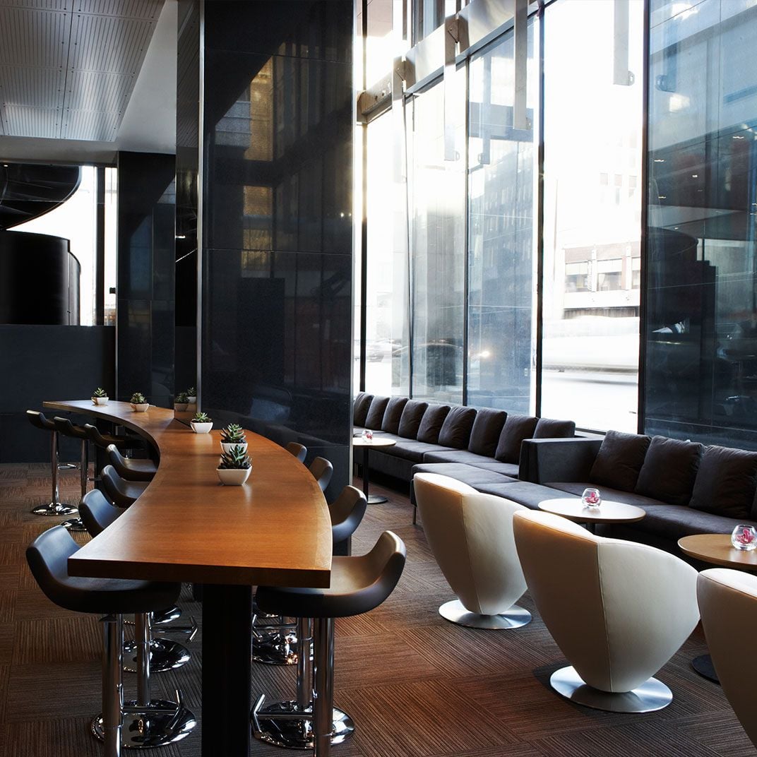 Floor-to-ceiling windows flood the hotel's modern restaurant with natural light, where sleek banquettes and sculptural cream chairs create an sophisticated urban dining atmosphere.