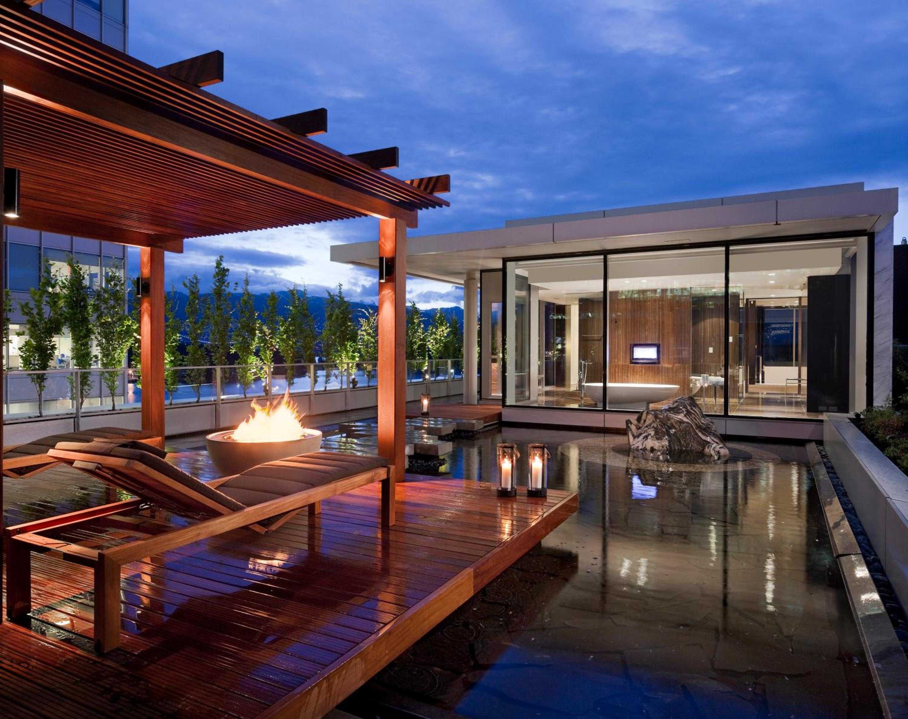 Flames dance in a sculptural fire bowl as twilight paints the sky, while warm wood pergolas frame this sophisticated rooftop sanctuary above Vancouver's harbor.