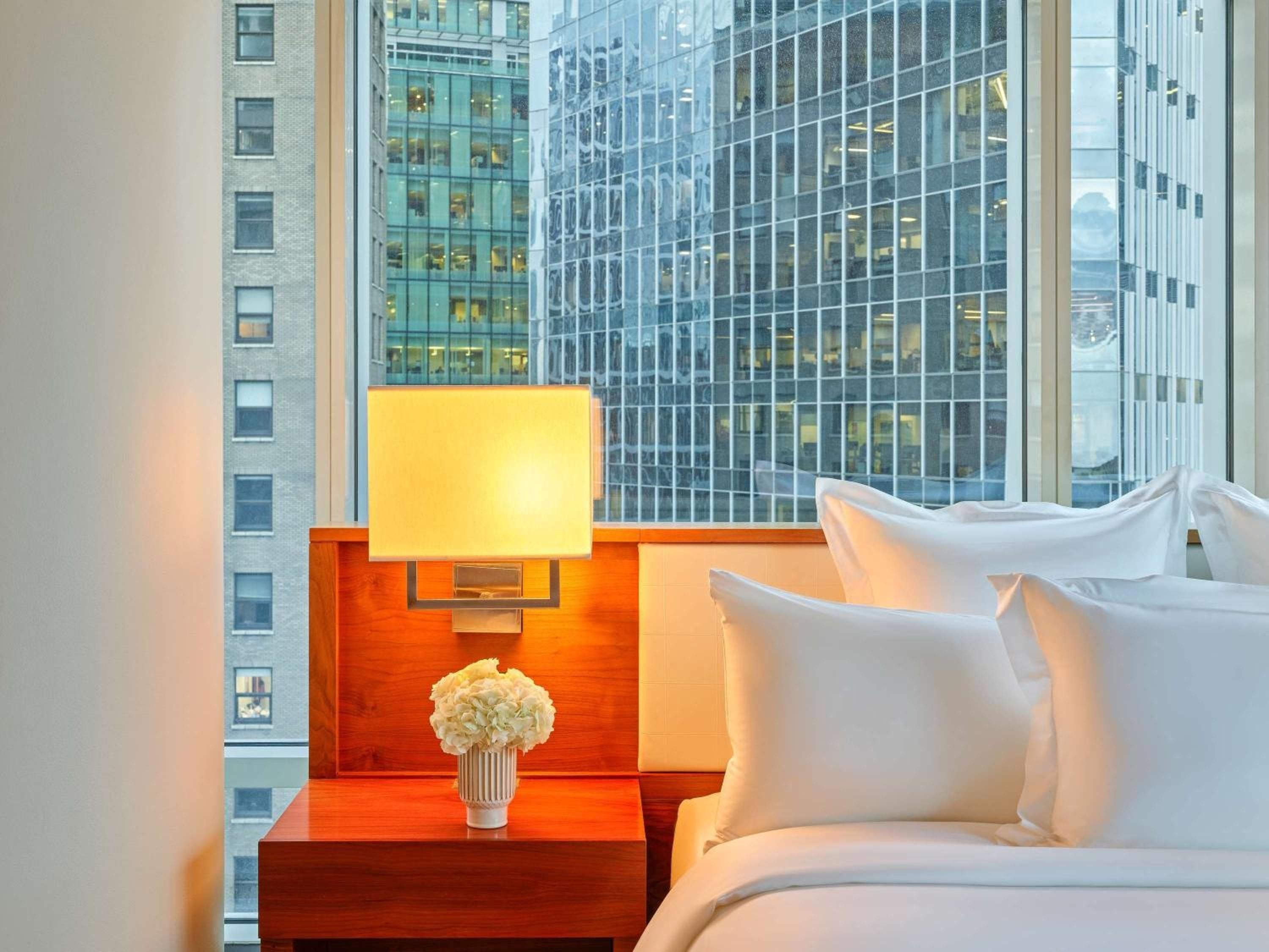 Crisp white linens meet warm amber lighting beside floor-to-ceiling windows showcasing Vancouver's glittering downtown towers, creating an intimate urban sanctuary.