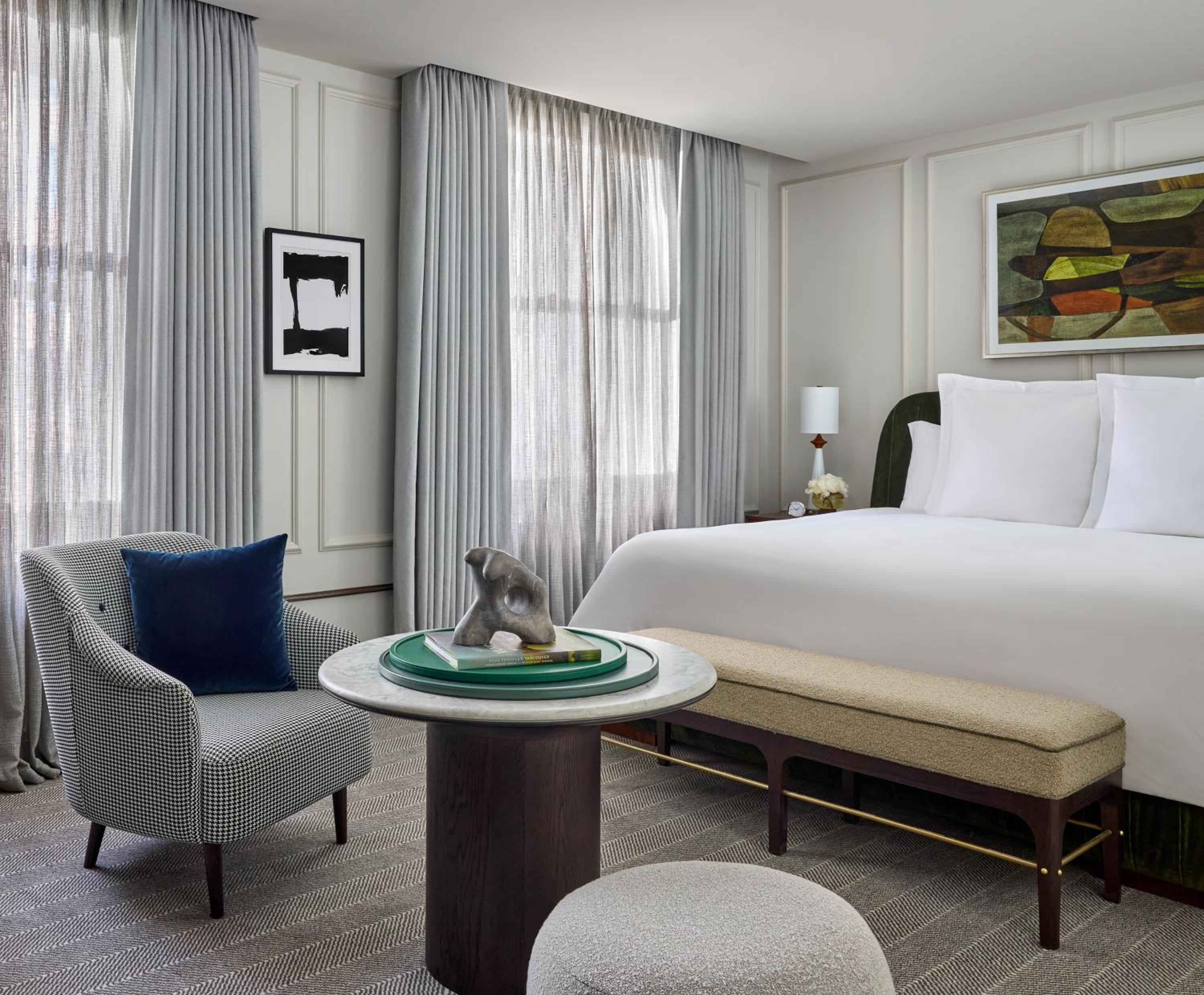 Sophisticated mid-century furnishings and curated artwork create an intimate sanctuary, where houndstooth armchairs and marble-topped tables invite quiet contemplation beside floor-to-ceiling windows.
