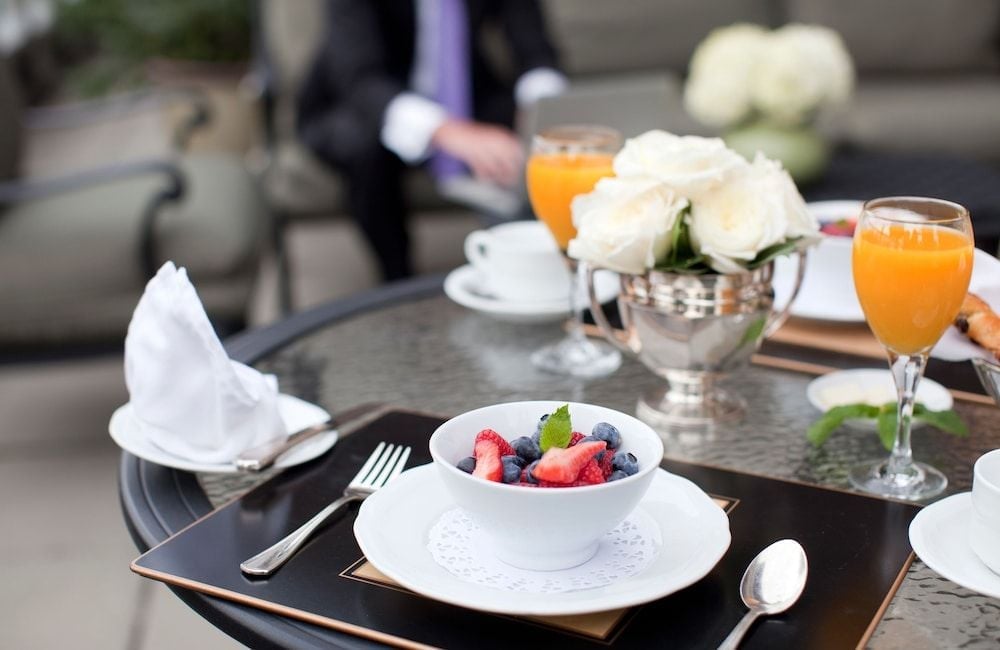 Fresh berries and orange juice arrive on gleaming silver at this intimate downtown Vancouver retreat, where afternoon light dances across polished surfaces and white roses.