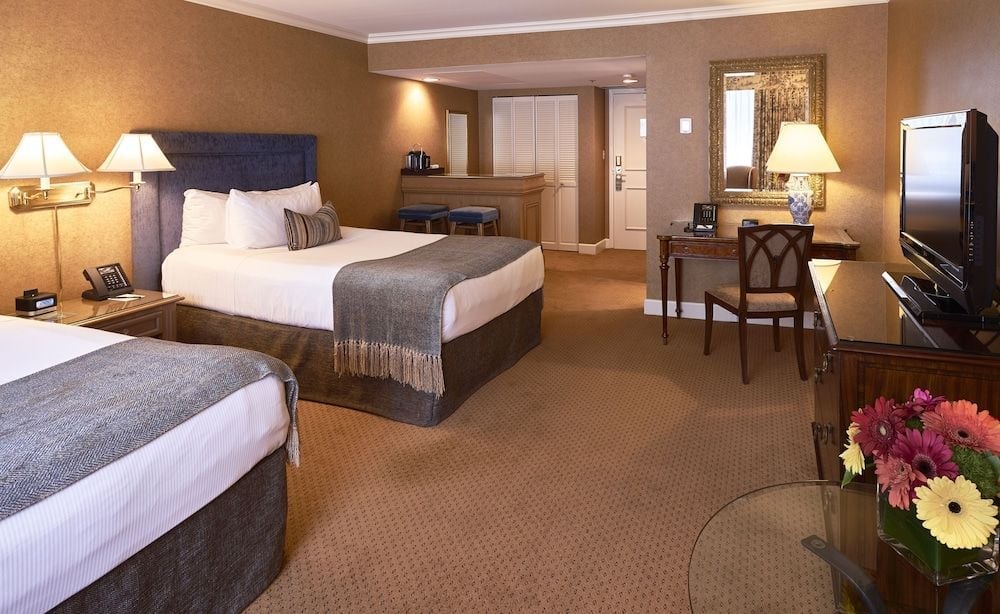 Warm amber lighting bathes this sophisticated double room, where navy headboards and rich wood furnishings create an inviting retreat with thoughtful touches like fresh gerbera daisies.