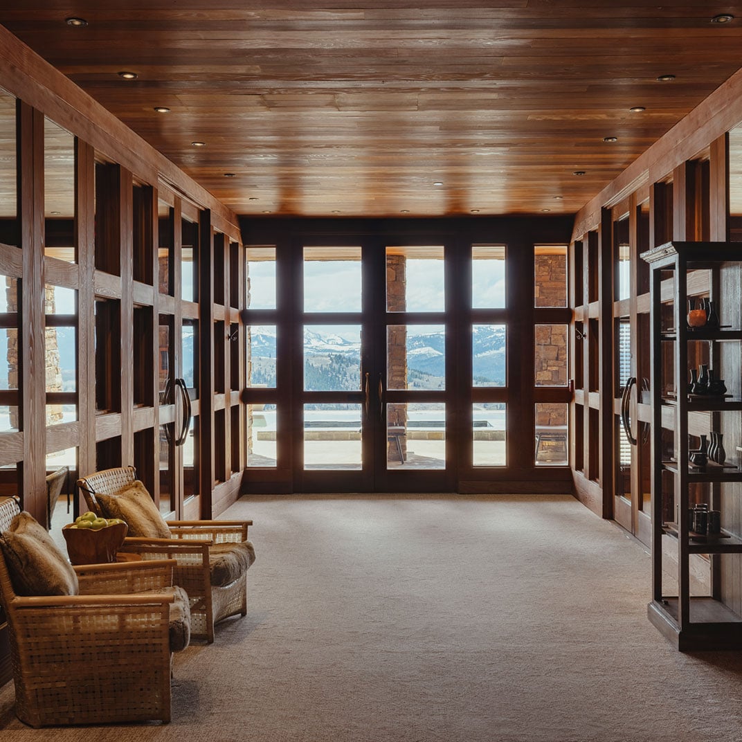 Handcrafted timber bunks line this rustic retreat space, where recessed lighting casts warm shadows and floor-to-ceiling windows frame the dramatic Teton wilderness beyond.