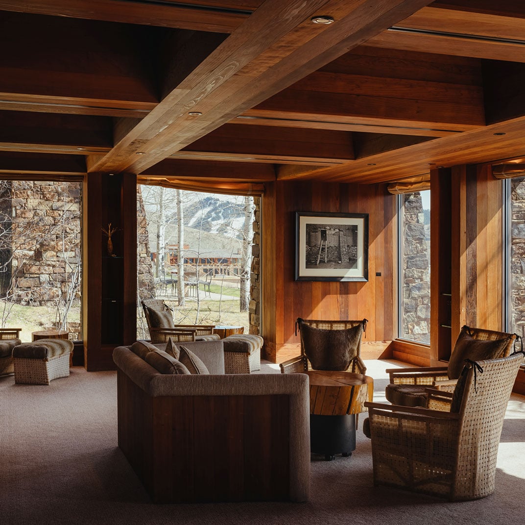 Exposed timber beams frame a contemplative living space where woven chairs and plush sofas invite lingering conversations beneath Wyoming's snow-dusted peaks.