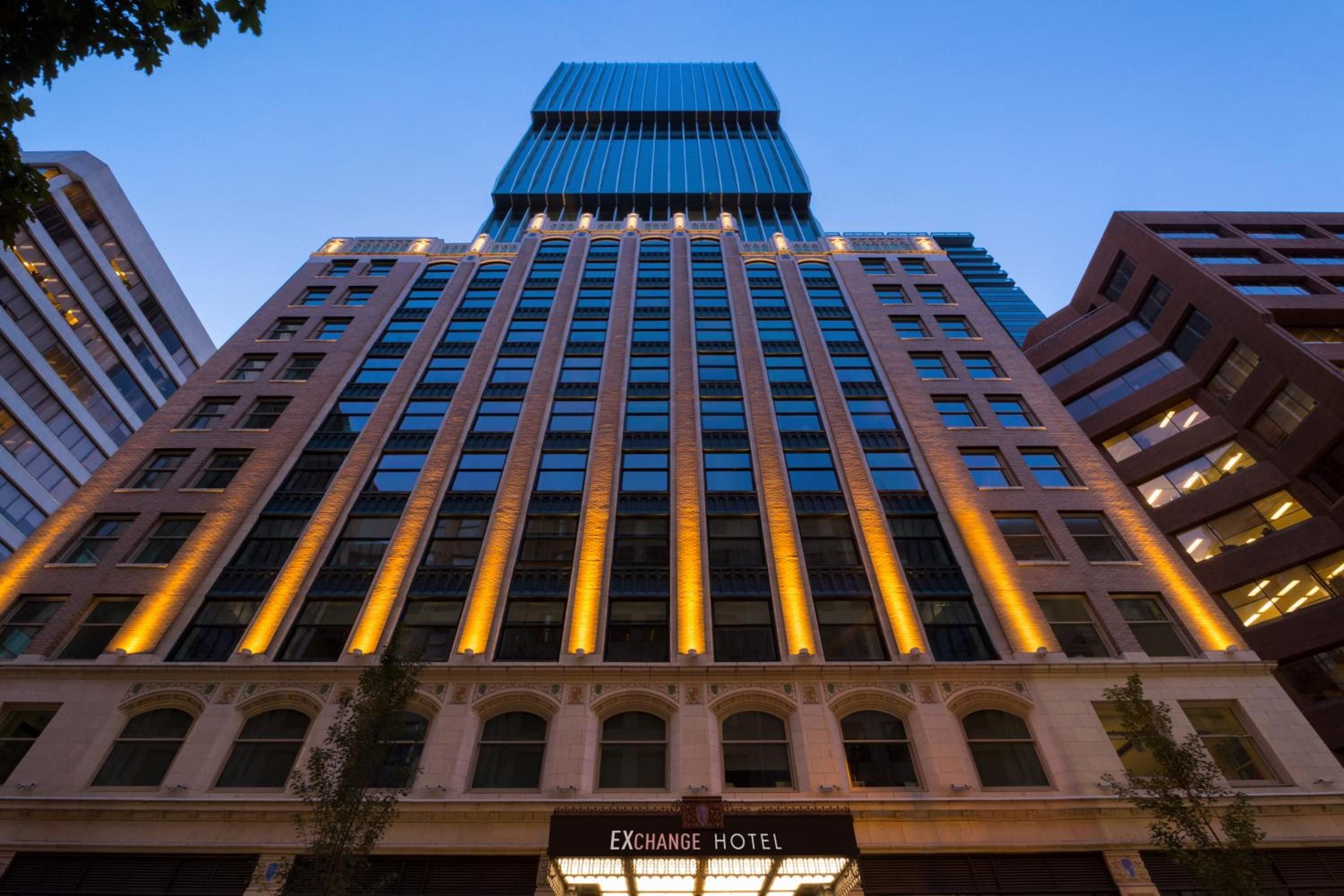 Dramatic uplighting illuminates the brick facade's towering columns as twilight settles over downtown Vancouver, creating an elegant beacon amid the urban streetscape.