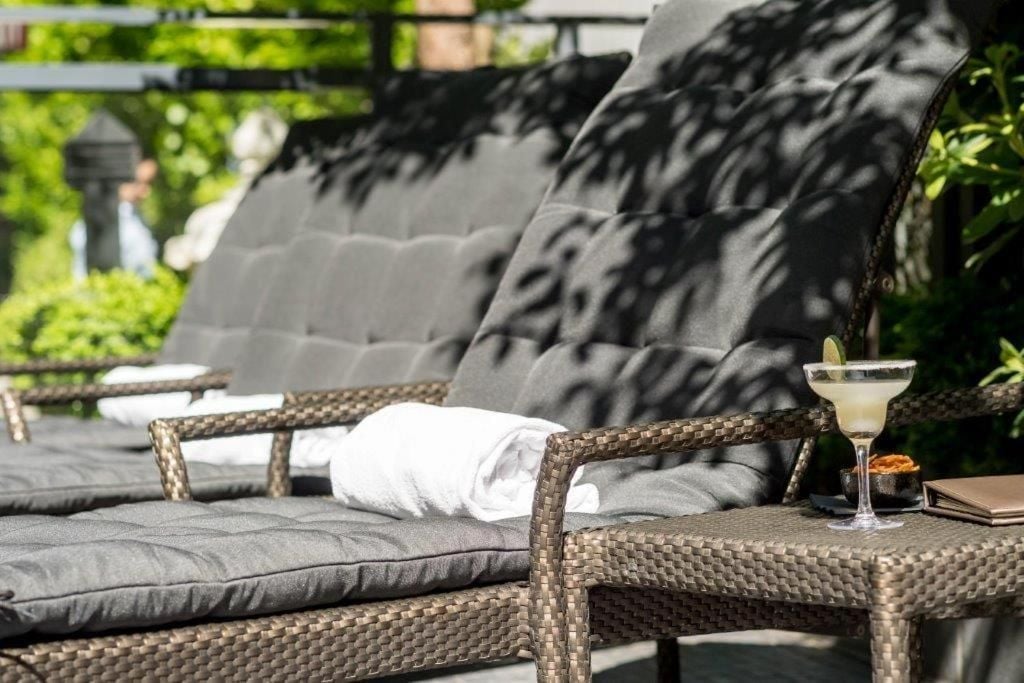Wicker loungers with plush gray cushions invite afternoon repose, where dappled shadows dance and chilled cocktails await within arm's reach of perfectly positioned side tables.