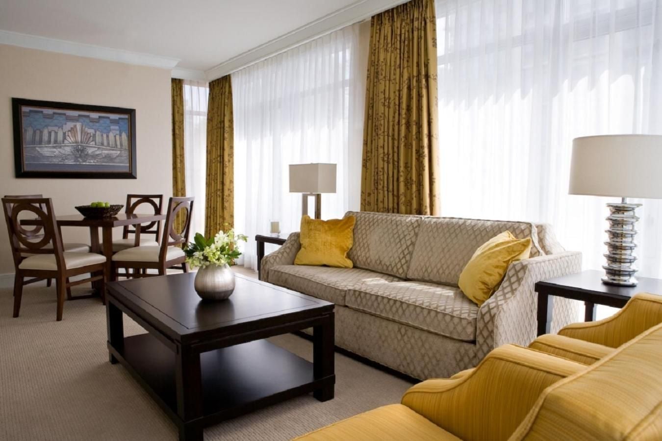 Golden silk curtains frame floor-to-ceiling windows while mustard velvet chairs complement the sophisticated gray sofa, creating an elegant living space bathed in natural light.