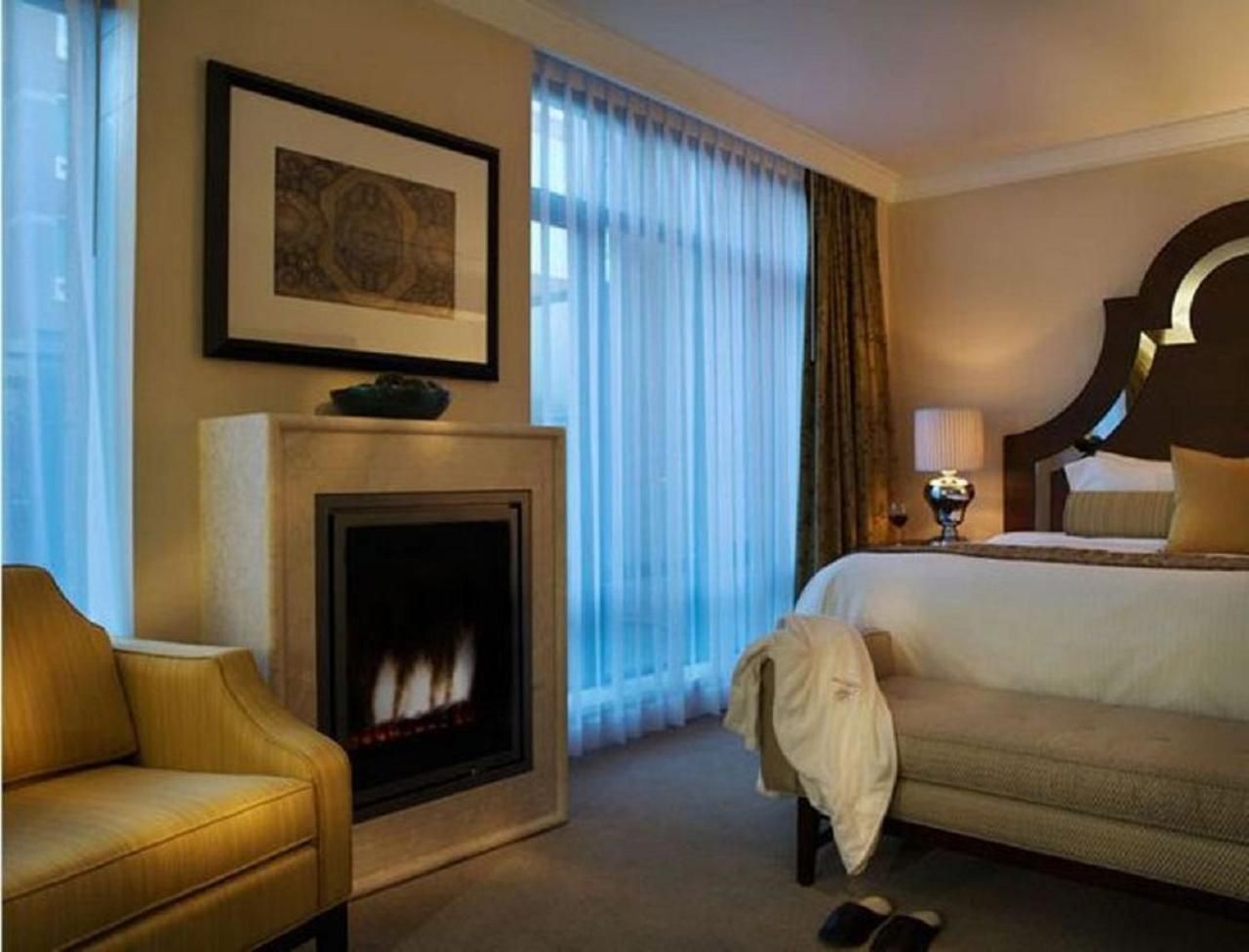 Flickering flames cast intimate shadows across cream walls while golden lamplight creates the perfect ambiance for evening relaxation in this thoughtfully appointed guest room.