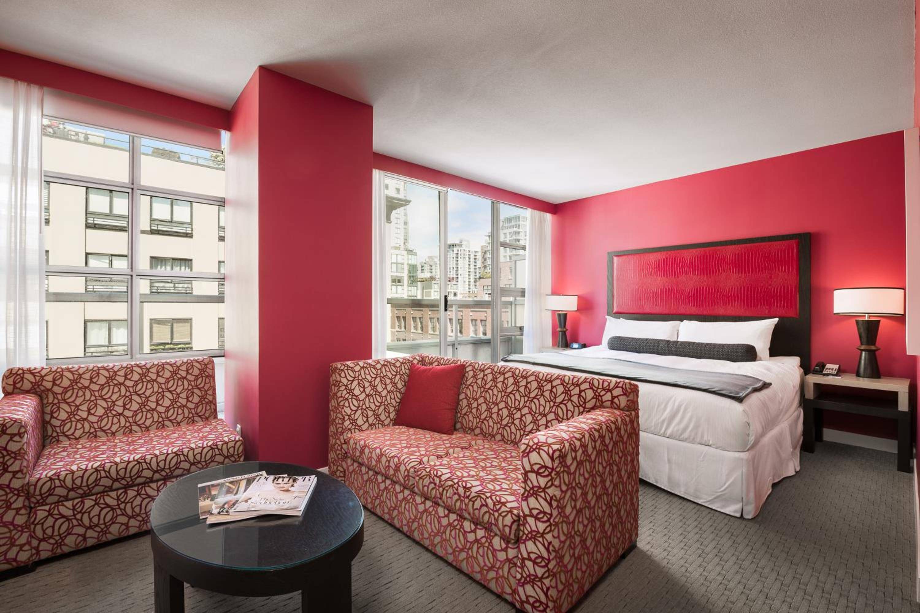 Bold crimson walls frame corner windows overlooking the city, while geometric-patterned seating creates an intimate lounge area within this striking urban suite.
