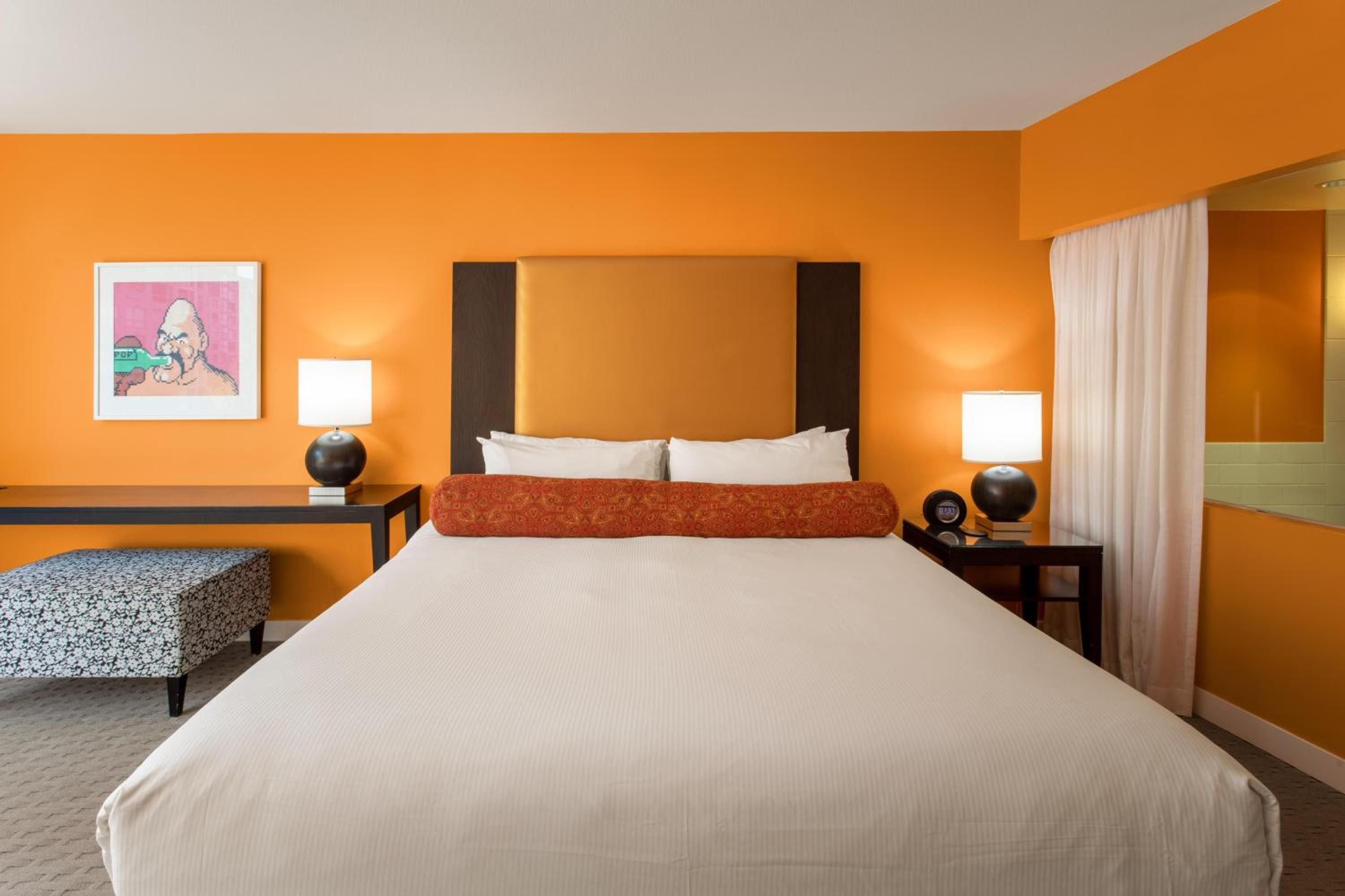 Bold tangerine walls create an energizing cocoon around crisp white linens, while spherical bedside lamps cast a warm glow across this thoughtfully designed urban retreat.