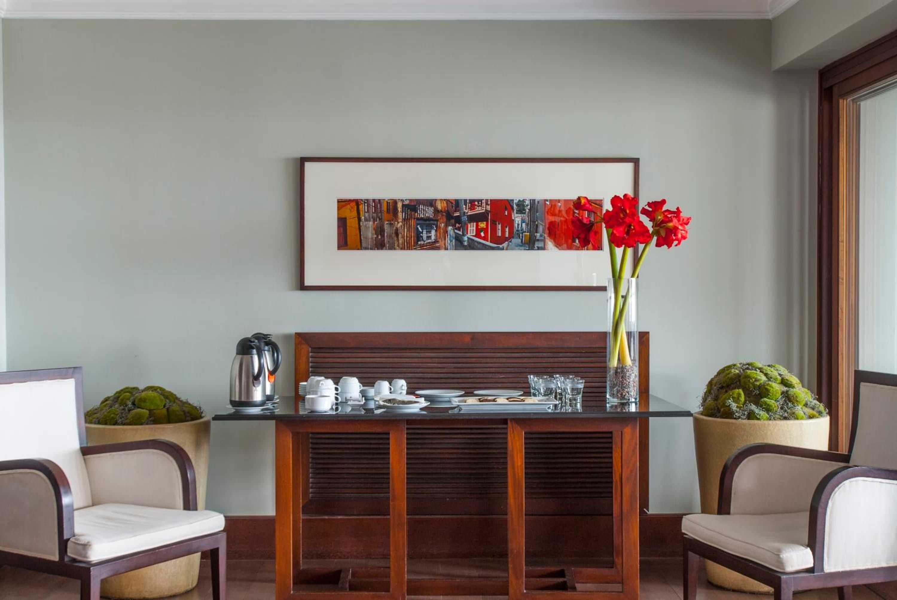 Warm wood furnishings and vibrant red amaryllis create an inviting coffee station, where sleek modern design meets thoughtful hospitality touches in this elegant guest lounge.