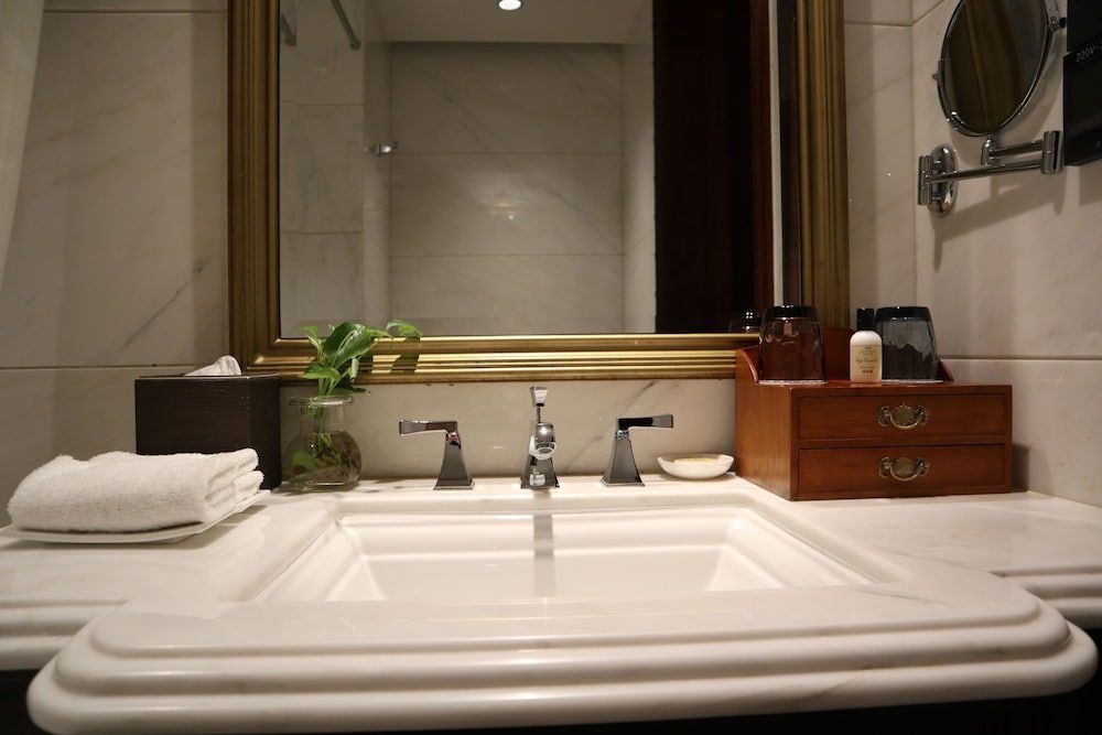 Polished marble surfaces and warm wood accents frame the pristine vanity, where carefully curated amenities and fresh greenery create an intimate spa-like sanctuary.