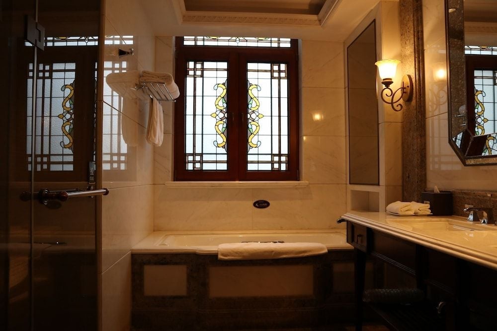 Warm amber light filters through Art Deco stained glass, casting golden hues across marble surfaces where modern luxury meets Shanghai's storied architectural heritage.