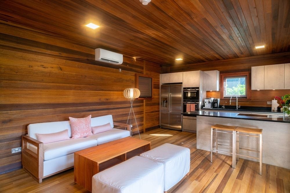 Warm wood paneling envelops the open-plan living space, where contemporary furnishings and natural textures create an intimate retreat above the Caribbean canopy.