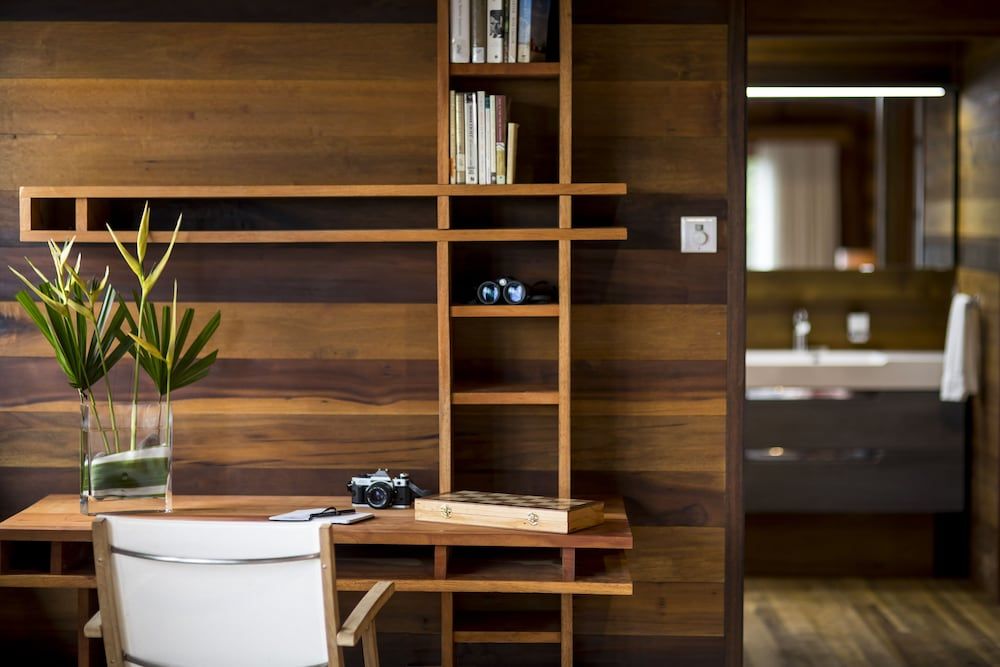 Warm teak shelving and integrated workspace create intimate moments of productivity, where vintage cameras and tropical foliage blend seamlessly with modern minimalist design.