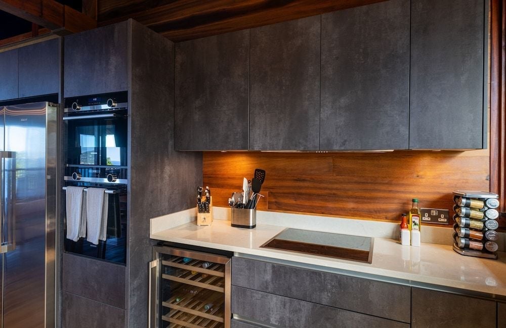 Sleek concrete cabinetry and warm wood backlighting create an unexpectedly sophisticated culinary workspace, where modern minimalism meets tropical luxury in this villa's designer kitchen.