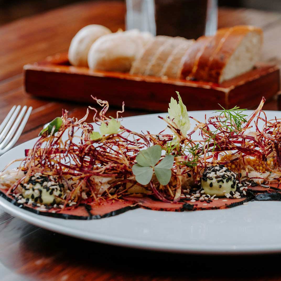 Artfully plated tataki arrives adorned with delicate microgreens and crimson threads, while warm bread waits nearby—a symphony of textures and Japanese precision.