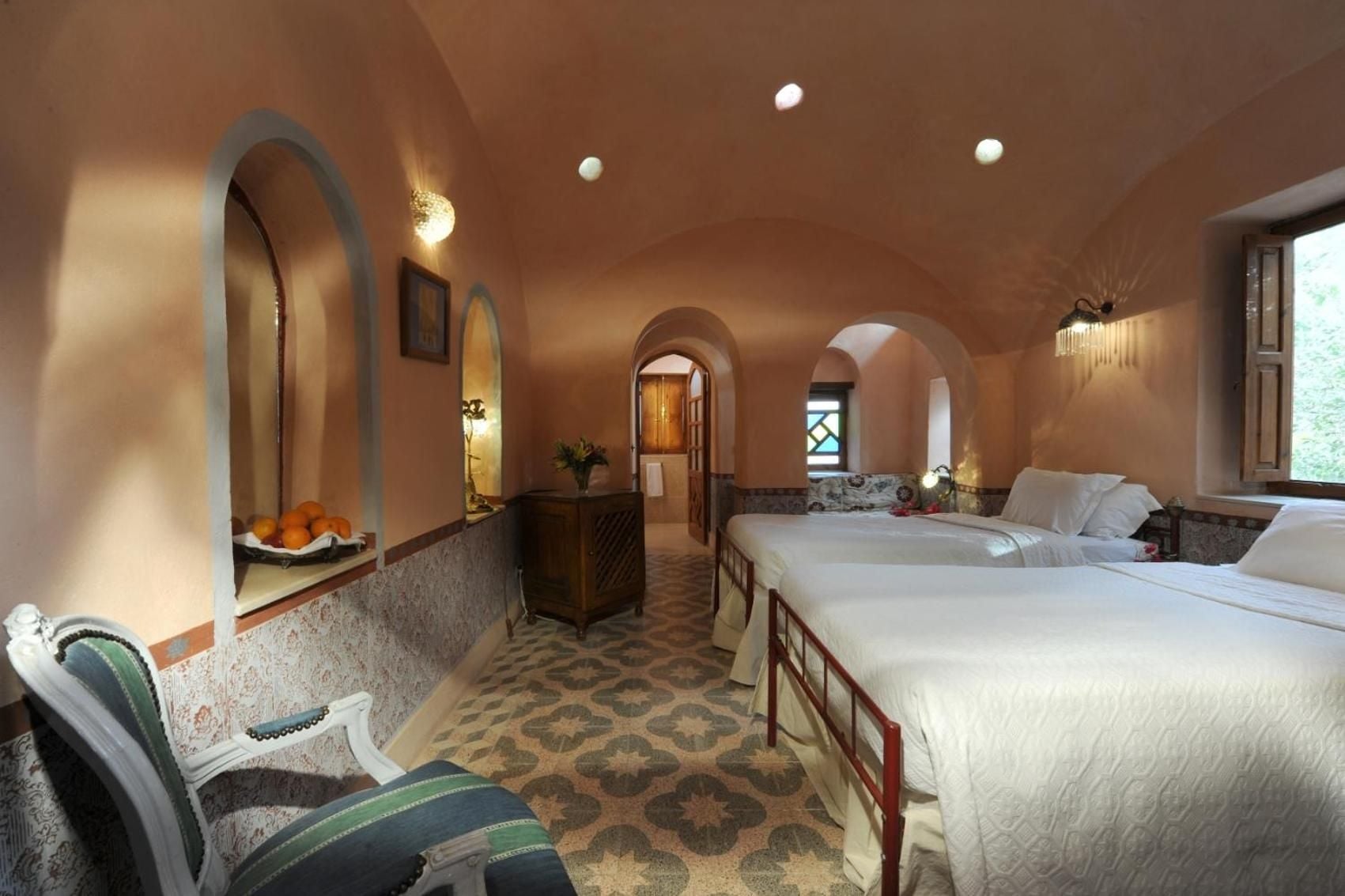 Arched doorways and handpainted tiles create an authentic Moorish sanctuary, where twin beds rest beneath vaulted ceilings warmed by amber light and desert hues.