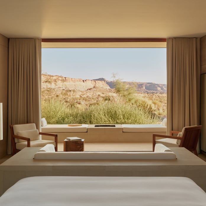 Floor-to-ceiling windows frame Utah's dramatic mesa landscape from minimalist suites, where warm wood furnishings and neutral linens create serene sanctuary amid the desert's raw beauty.